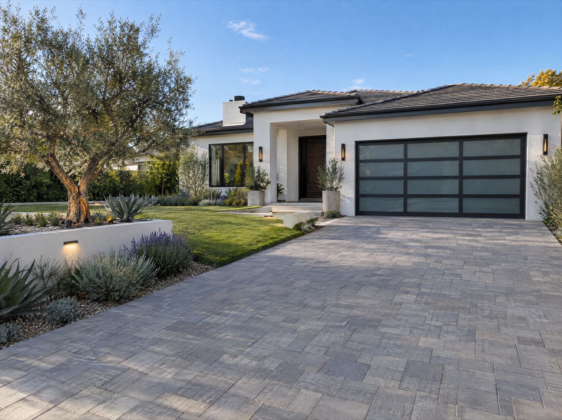 Grey paver driveway, lawn and lit planter walls at a modern home